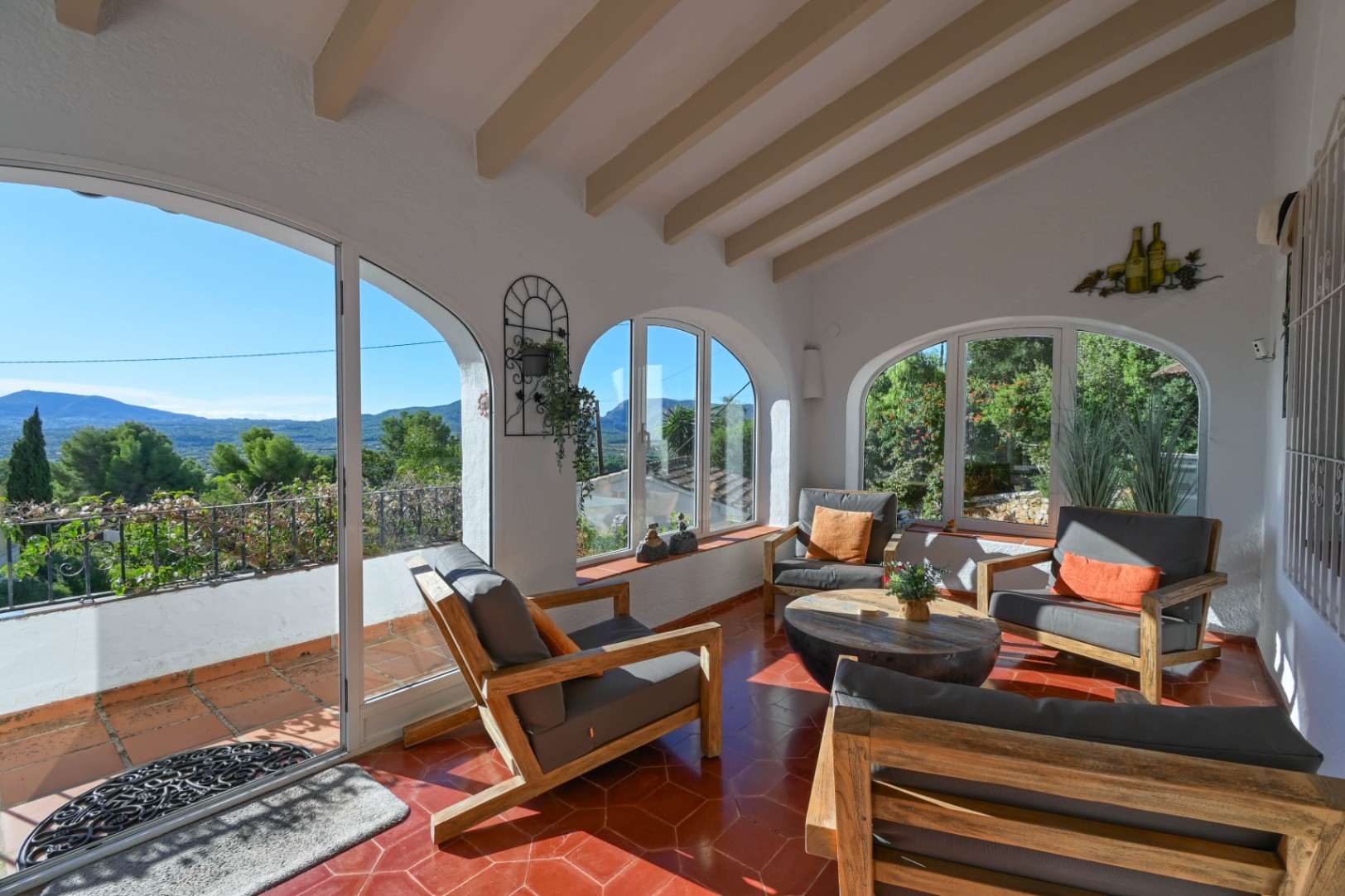 Terraza acristalada con vigas de madera, suelo de terracota hexagonal y ventanales en arco con vistas despejadas a las montañas y el valle.