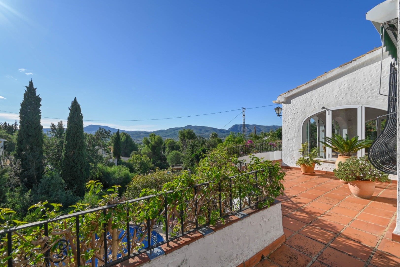 Terraza elevada con suelo de terracota y barandilla de forja, con vistas panorámicas a las montañas y al frondoso valle mediterráneo.