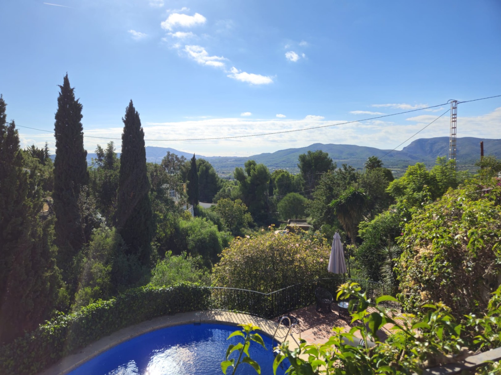 Vista elevada de una piscina curva y terraza de terracota, rodeada de cipreses con vistas panorámicas al valle y las montañas circundantes.