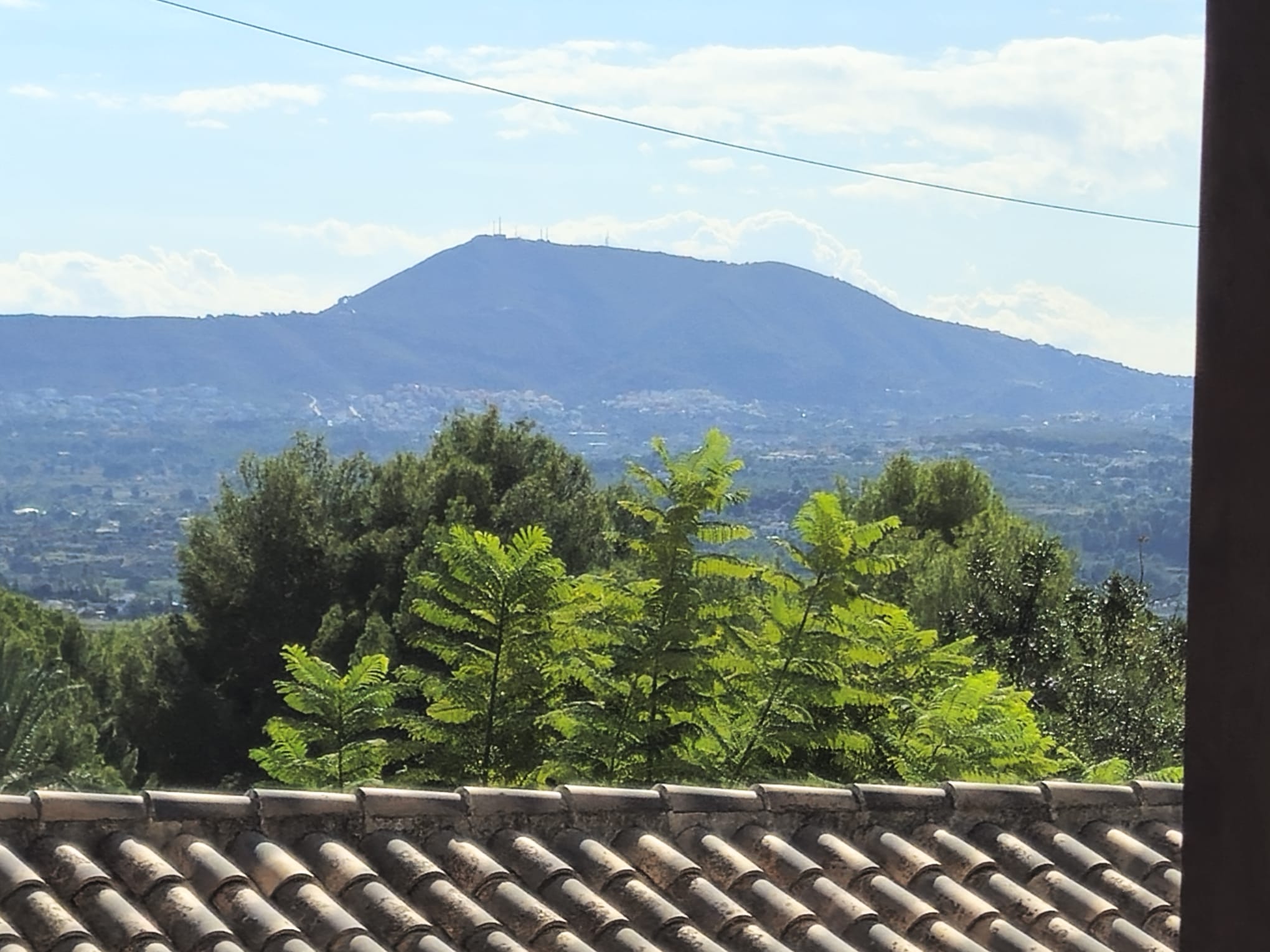 Vista panorámica desde la azotea con tejas de arcilla tradicionales, vegetación frondosa y una montaña prominente en el horizonte bajo un cielo despejado.