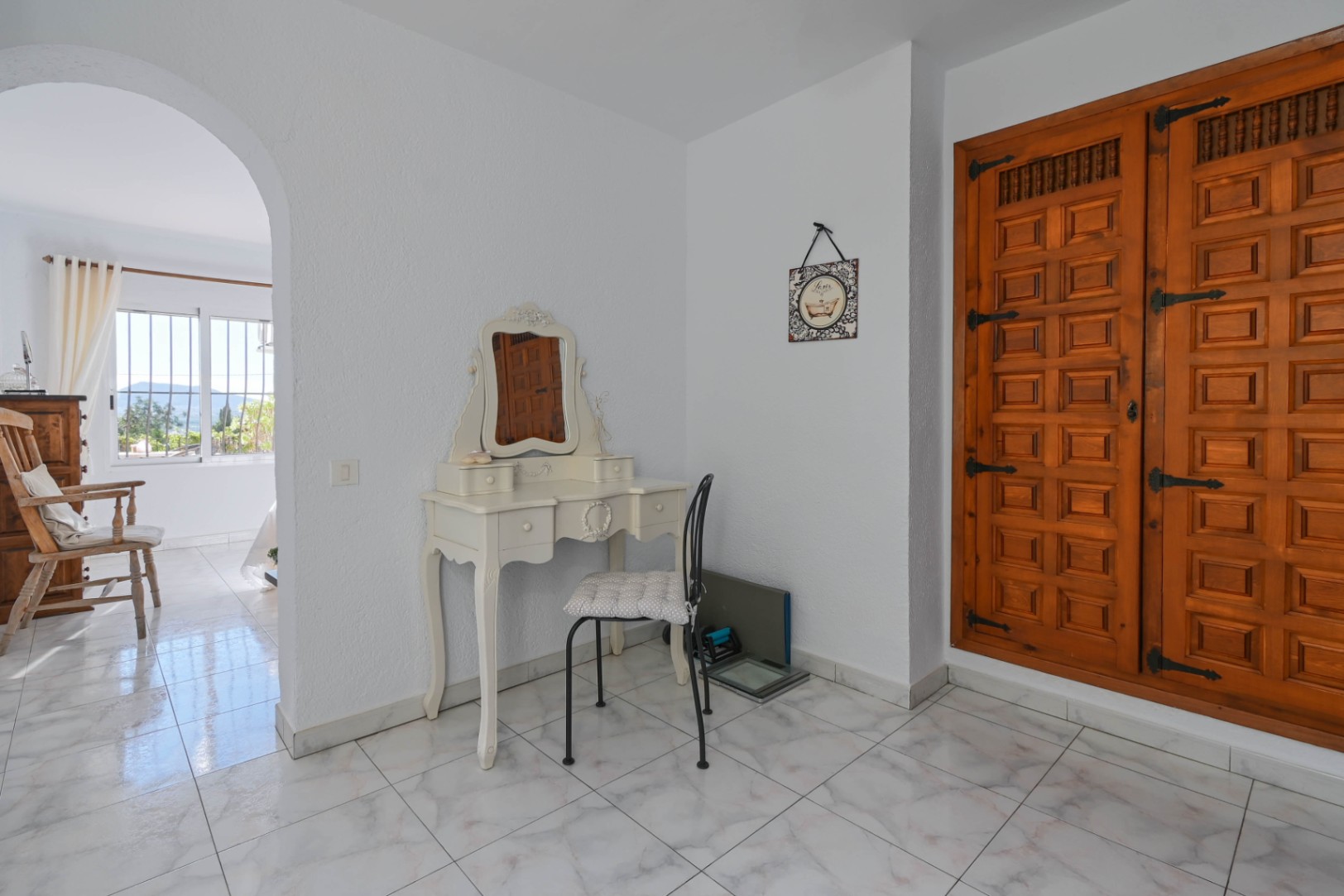 Zona de tocador con mesa blanca de estilo clásico y un gran armario empotrado de madera tallada con herrajes de hierro tradicionales sobre suelo cerámico.