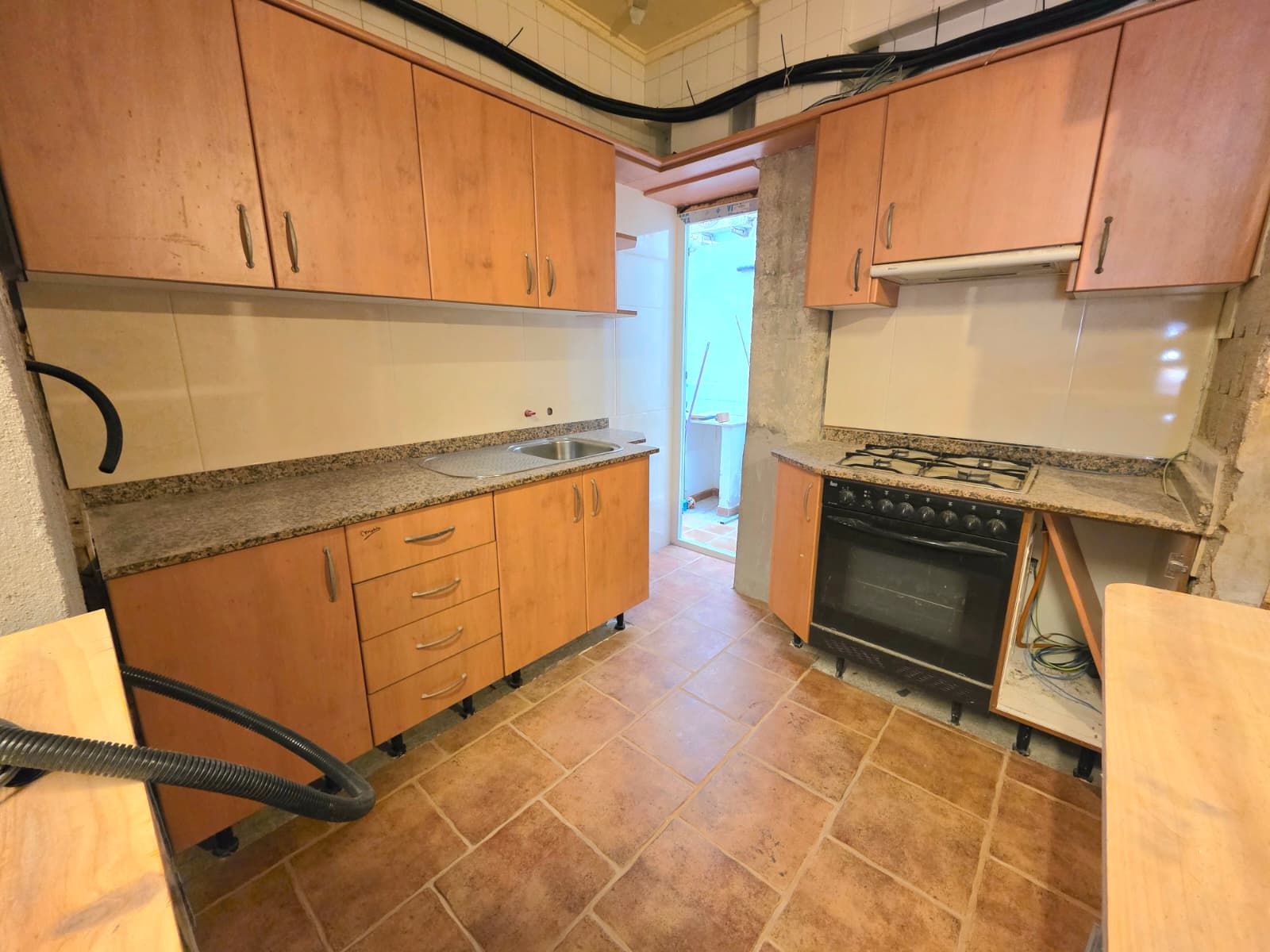 Cocina con armarios de acabado madera, encimeras de granito y suelos de gres rústico. Incluye placa de gas, horno integrado y acceso directo a un patio exterior.