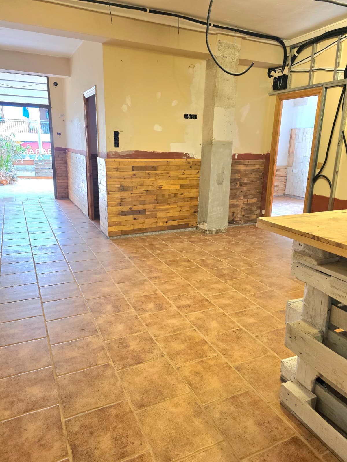 Espacio interior con suelos de gres en tonos tierra, friso de madera rústica y techos con instalaciones vistas, ideal para reforma o local comercial.