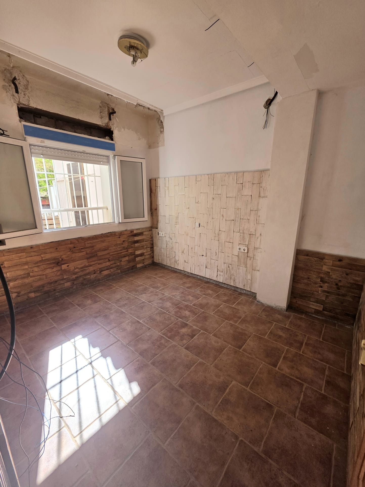 Habitación con suelo de baldosas cerámicas y paredes revestidas con paneles de madera decorativa. La luz natural ilumina el espacio en proceso de reforma.