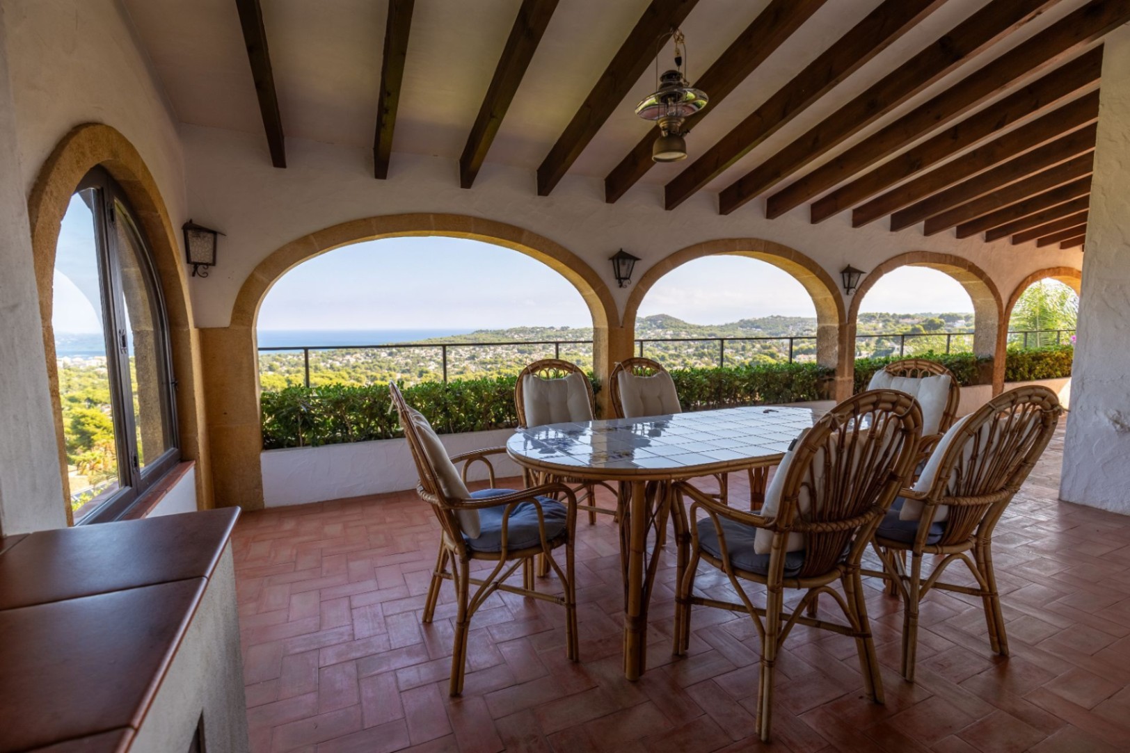 Terraza cubierta con arcos de piedra, vigas de madera y suelo de terracota. Dispone de comedor de mimbre con vistas panorámicas al paisaje mediterráneo y al mar.