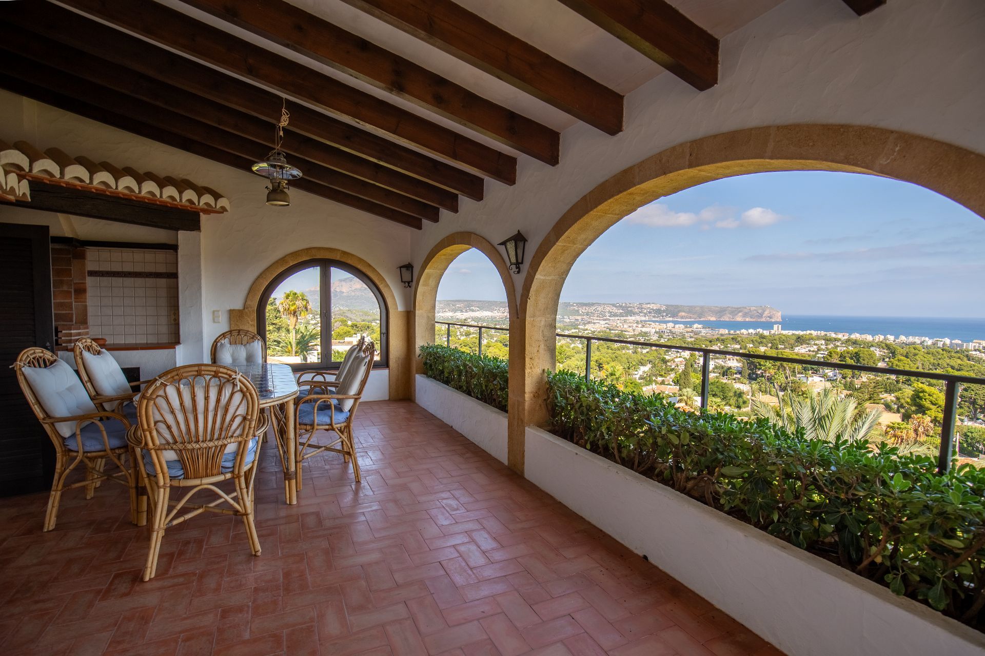 Terraza cubierta con vigas de madera, suelo de terracota y arcos de piedra que ofrecen vistas panorámicas de la costa y el mar.