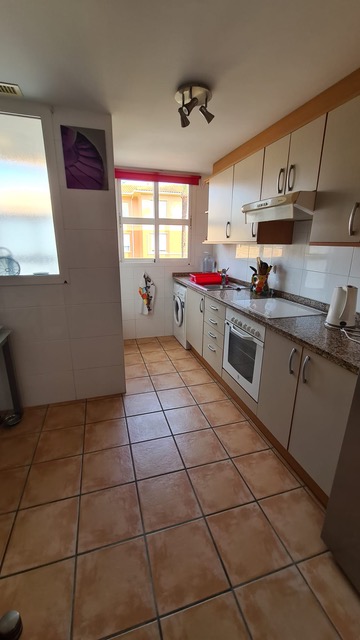 Cocina con suelos de gres rústico, encimera de granito y mobiliario en tono crema. Dispone de electrodomésticos integrados y luz natural a través de la ventana.