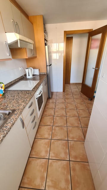 Cocina funcional con encimera de granito moteado, mobiliario blanco y suelos de gres cerámico. Incluye horno integrado y campana extractora.