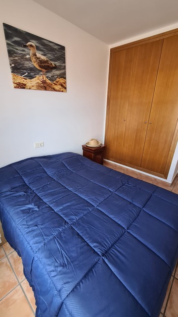 Dormitorio con armario empotrado de madera, cama con edredón azul y suelos de baldosa cerámica. Incluye una mesita de noche de madera y decoración de temática costera.