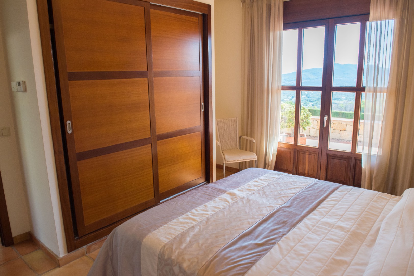 Dormitorio con armario empotrado de madera, puertas correderas y acceso directo a una terraza con vistas despejadas a la montaña.