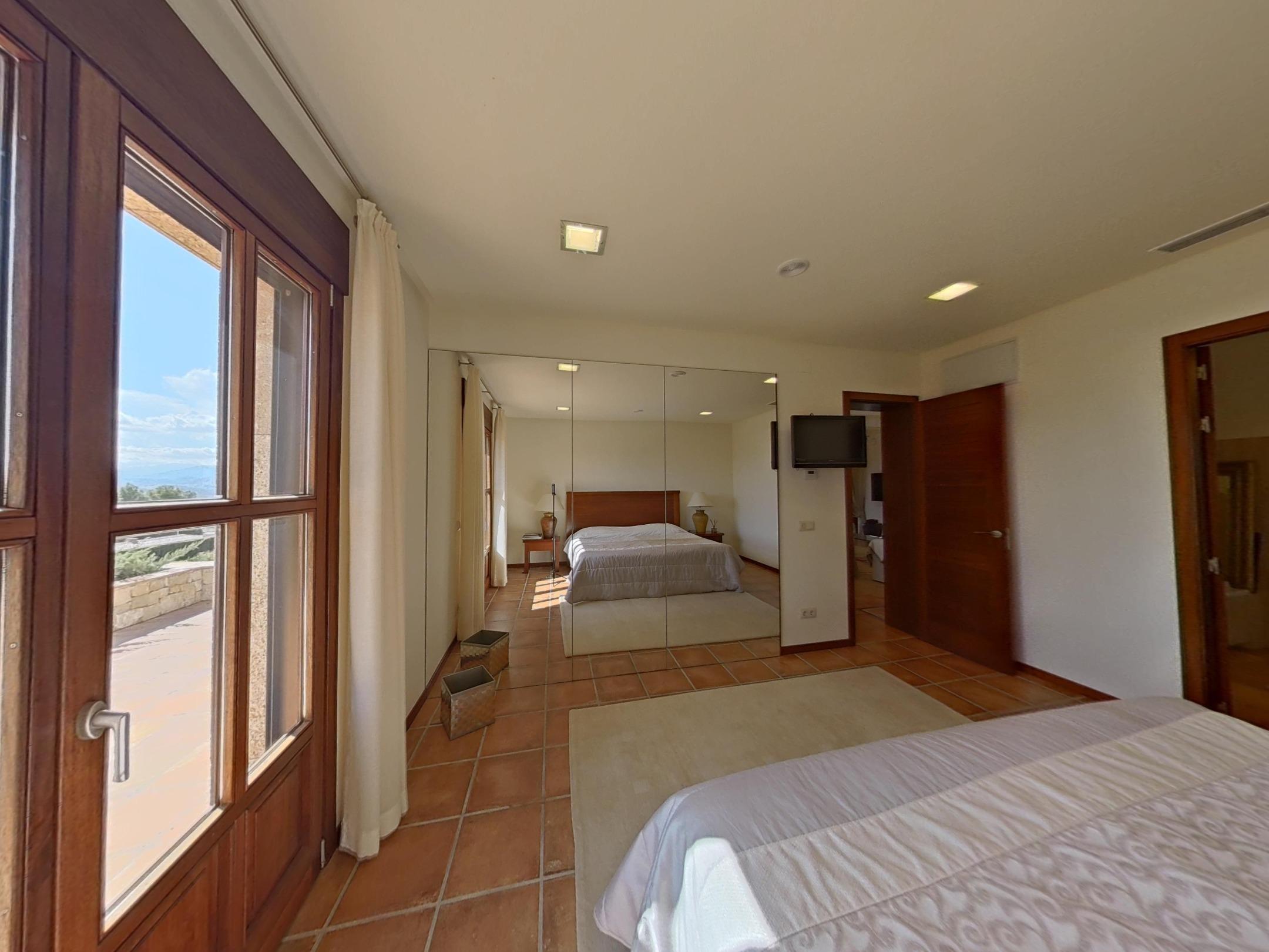 Dormitorio con suelos de barro cocido, armarios de espejo de suelo a techo y salida a terraza a través de carpintería de madera.