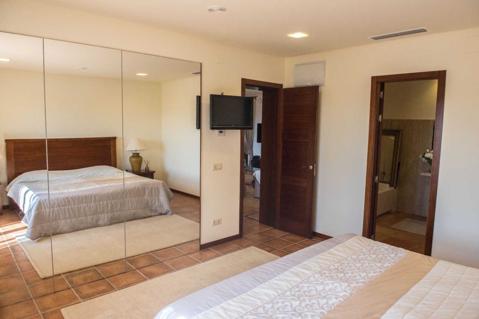 Dormitorio con suelos de terracota, un gran armario de espejos y televisión de pared. Dispone de iluminación empotrada y acceso directo a un cuarto de baño privado.
