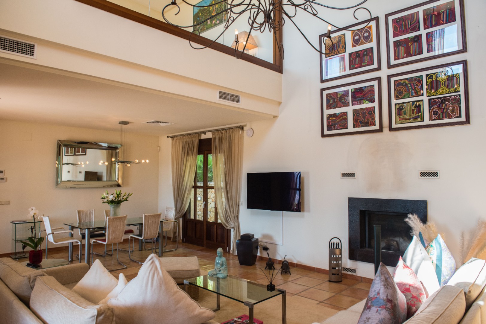 Salón de doble altura con suelos de terracota, chimenea de diseño negro, zona de comedor con mesa de cristal y una entreplanta con barandilla de vidrio.