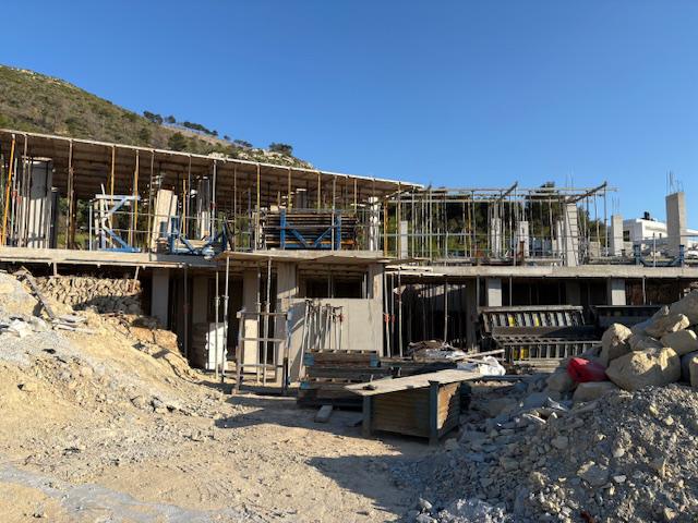 Estructura de hormigón armado en fase de construcción, con pilares, puntales metálicos y encofrados de madera integrados en un terreno montañoso.