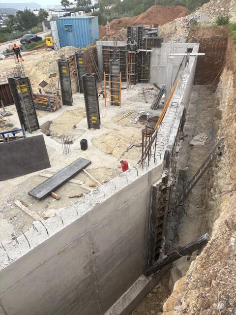 Fase de cimentación con muros de contención de hormigón armado y encofrados verticales para pilares estructurales en una parcela excavada.