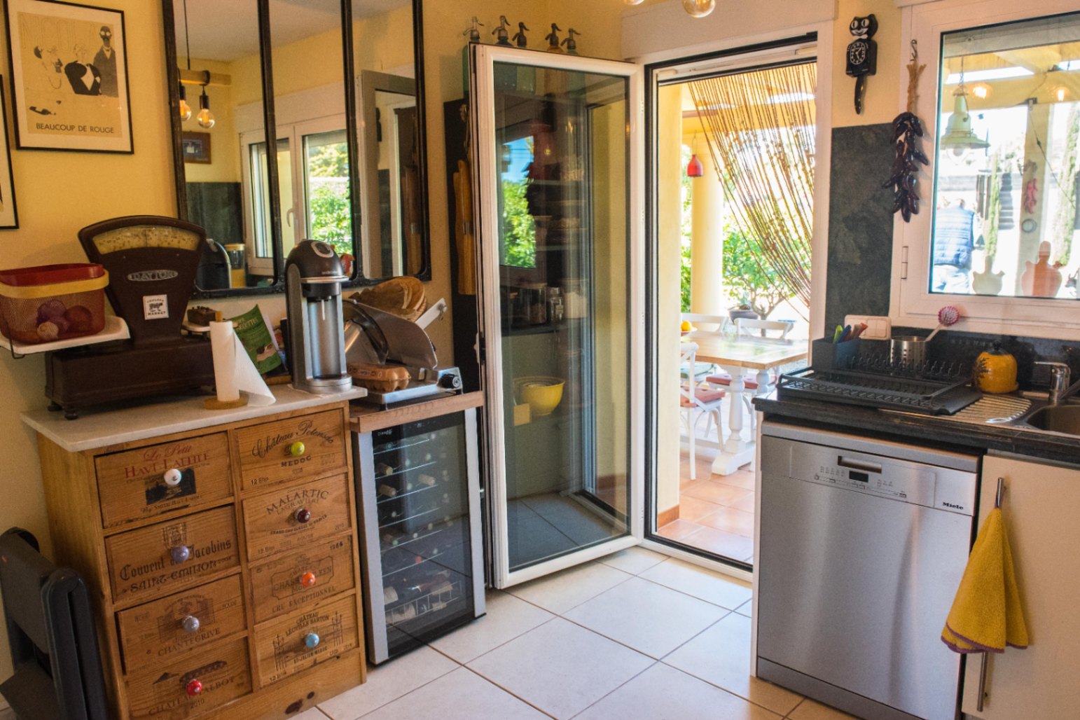 Rincón de cocina con cómoda de madera estilo caja de vino, vinoteca compacta y acceso directo a una terraza exterior amueblada a través de una puerta acristalada.