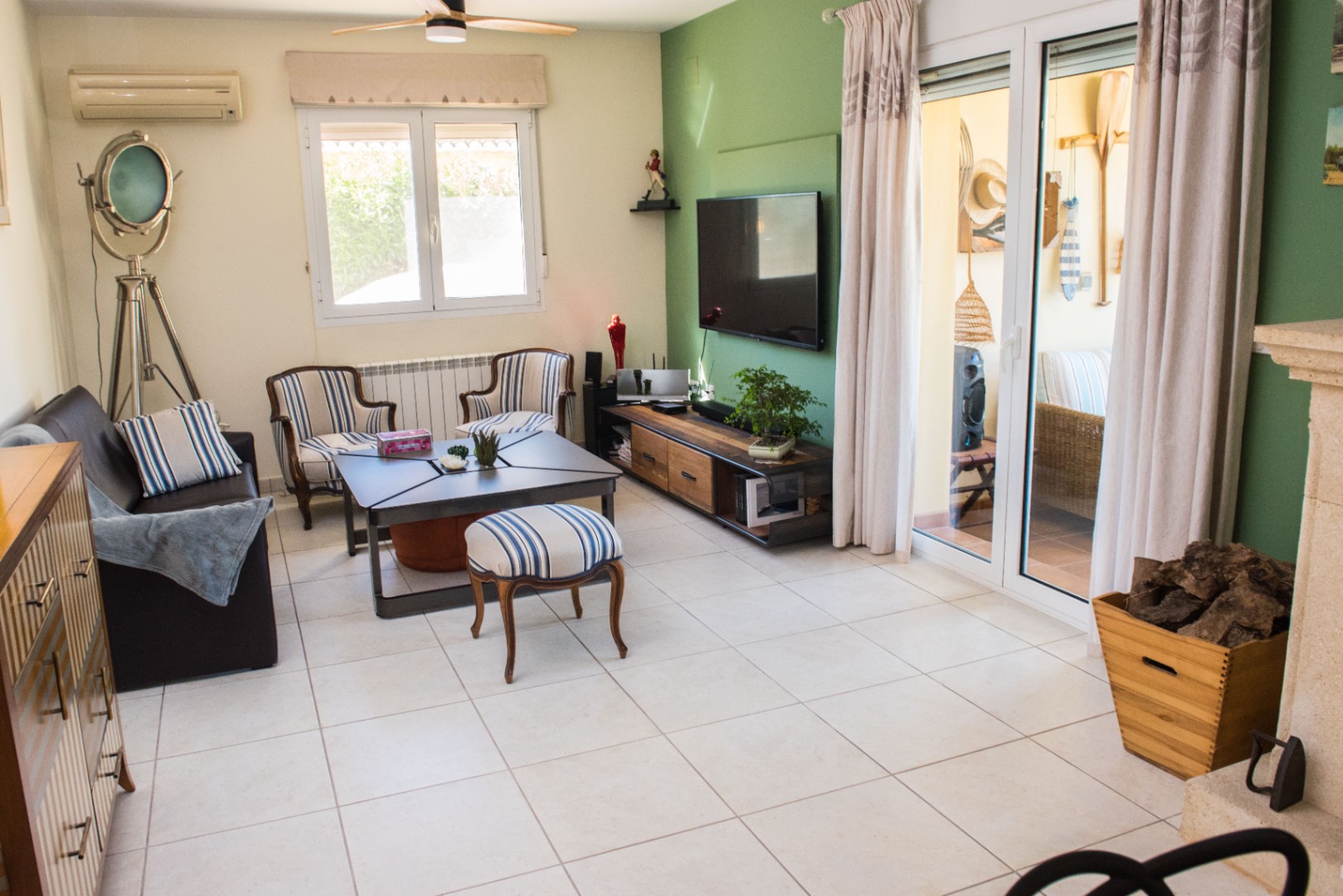 Salón con pared de acento verde, suelos cerámicos y mobiliario de inspiración náutica. Incluye una lámpara de trípode, aire acondicionado y acceso directo a la terraza.