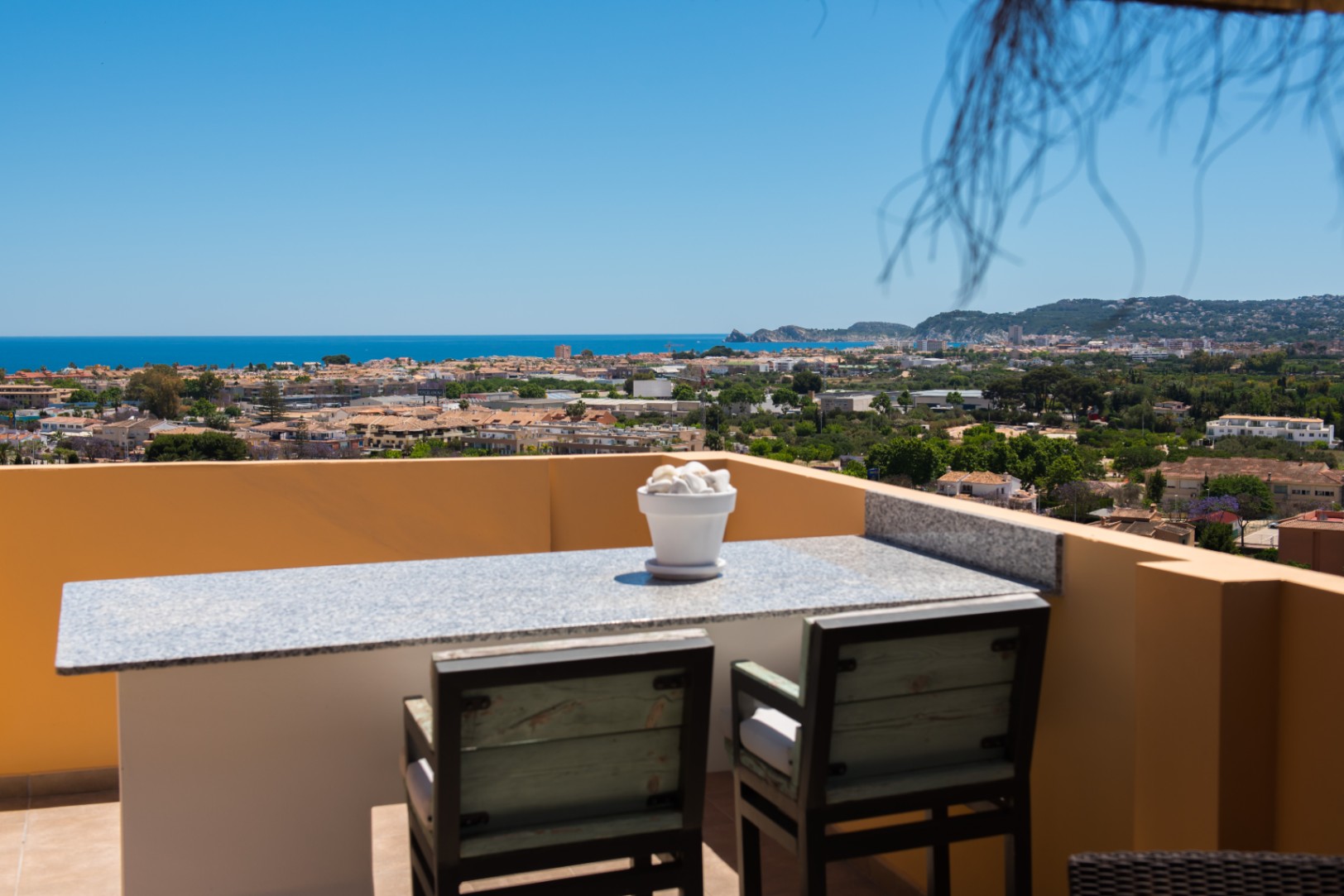 Terraza elevada con barra de granito y asientos de madera, que ofrece vistas panorámicas de la ciudad costera y el mar Mediterráneo bajo un cielo despejado.
