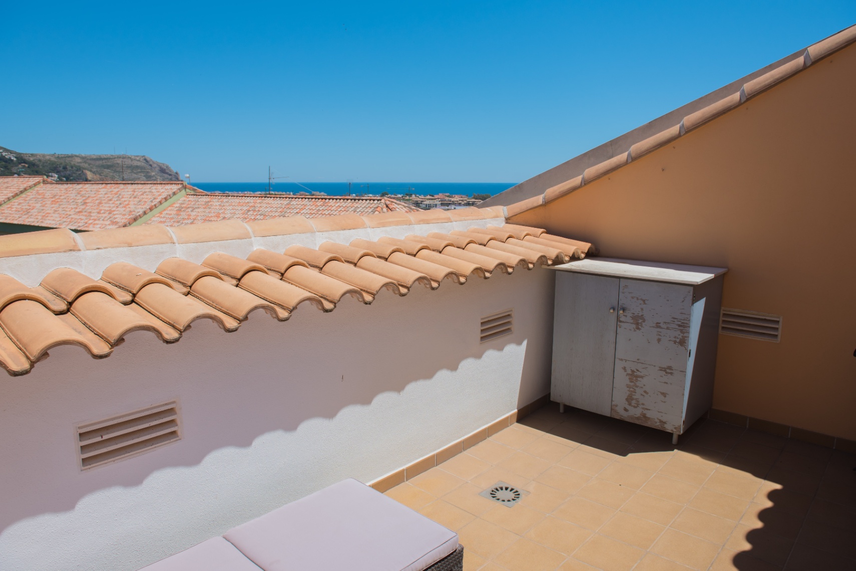 Terraza en azotea con suelos cerámicos, pretil de teja mediterránea y vistas al mar. Incluye un armario de almacenaje y rejillas de ventilación integradas.