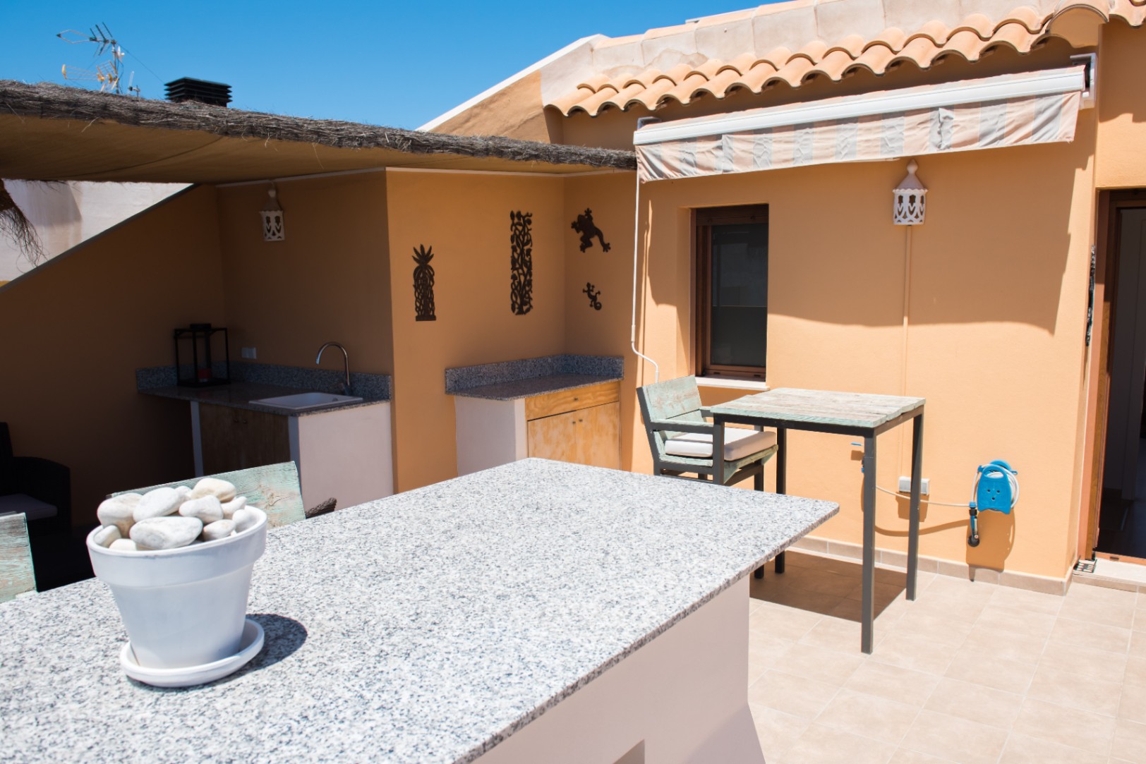 Terraza exterior con barra de granito, zona de fregadero integrada y armarios de madera rústica bajo un porche de brezo.