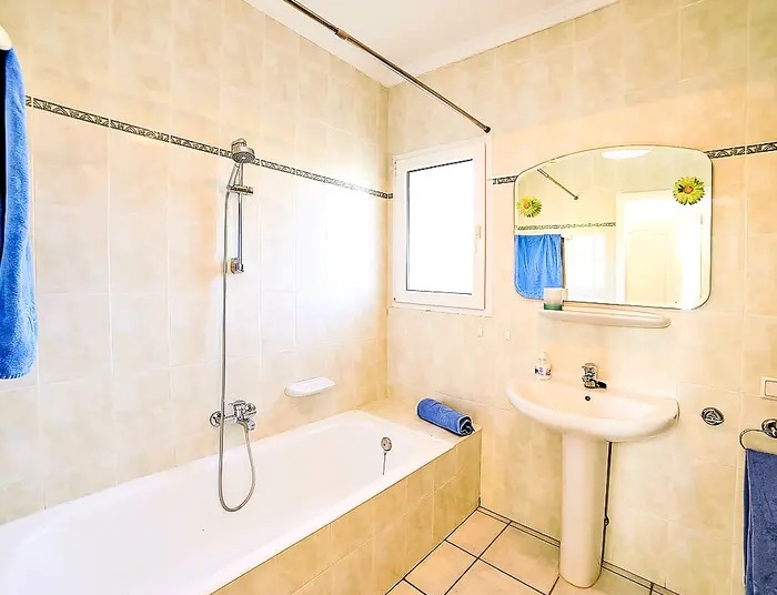 Cuarto de baño funcional con bañera, lavabo de pedestal y paredes alicatadas en tonos crema con una cenefa decorativa.