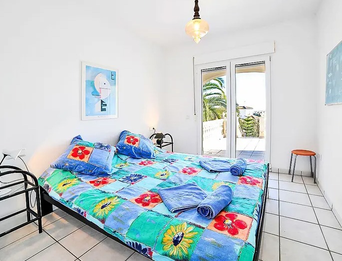 Dormitorio luminoso con suelos de baldosa blanca y acceso directo a una terraza privada con vistas a las palmeras y luz natural constante.