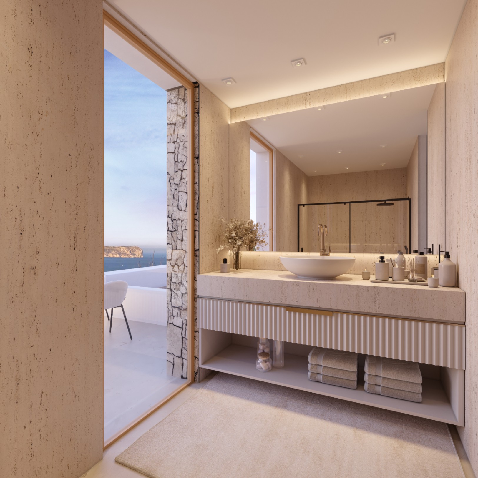Baño revestido en travertino con mueble suspendido estriado, lavabo sobre encimera y acceso directo a una terraza con vistas panorámicas al mar.