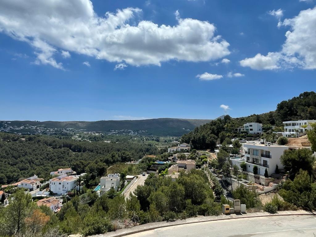 Vista elevada de un valle mediterráneo con villas blancas integradas en un denso pinar bajo un cielo despejado.