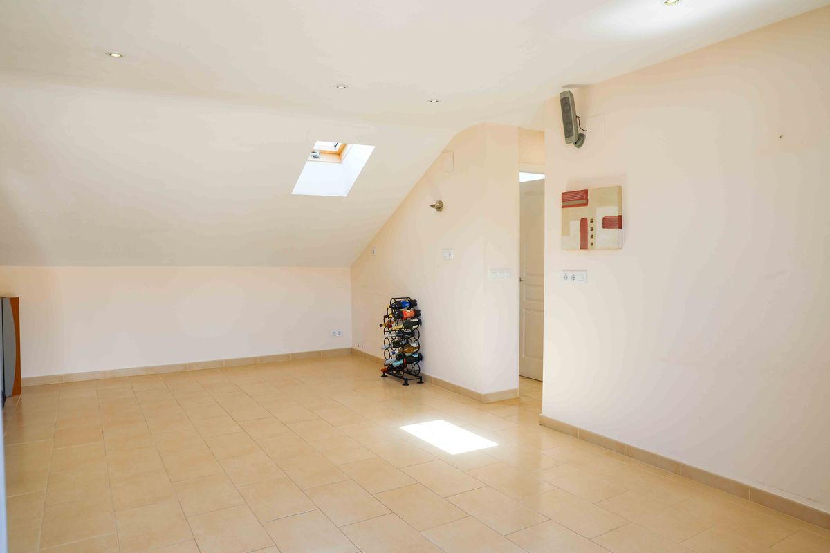 Amplia buhardilla con techos inclinados, ventana de tejado, suelos de gres en tonos beige e iluminación empotrada.