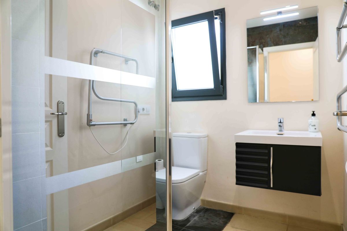 Baño moderno con mampara de ducha de cristal esmerilado, mueble de lavabo suspendido en color negro y radiador toallero cromado.