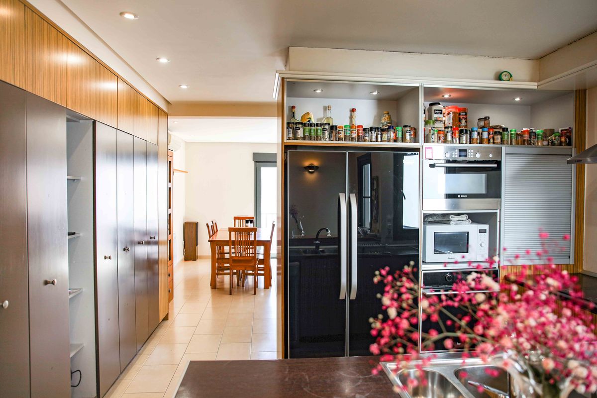 Cocina moderna con electrodomésticos integrados, frigorífico negro de doble puerta y amplios armarios de almacenaje que conectan con un comedor de madera.