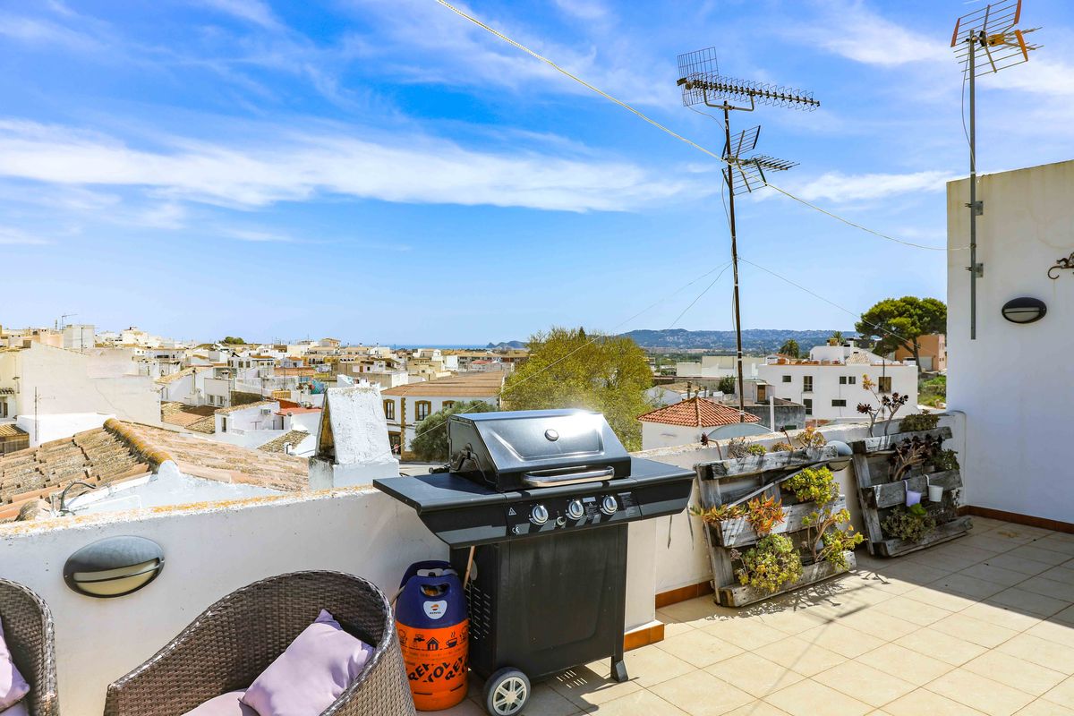 Terraza en la azotea con barbacoa de gas, asientos de mimbre y jardines verticales de palets, con vistas panorámicas al pueblo, las montañas y el mar.