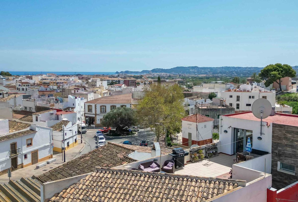 Vista elevada de un pueblo mediterráneo con una terraza privada equipada con barbacoa y mobiliario, ofreciendo vistas panorámicas al mar y los tejados.