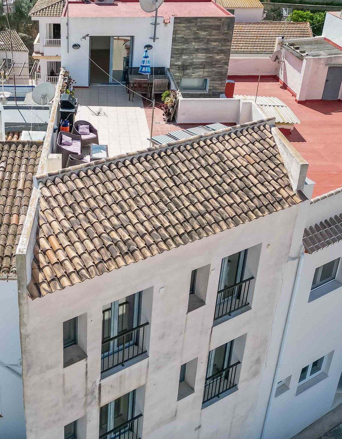 Vista exterior de un edificio blanco con tejado de teja tradicional y una terraza privada equipada con mobiliario de exterior y zona de comedor.
