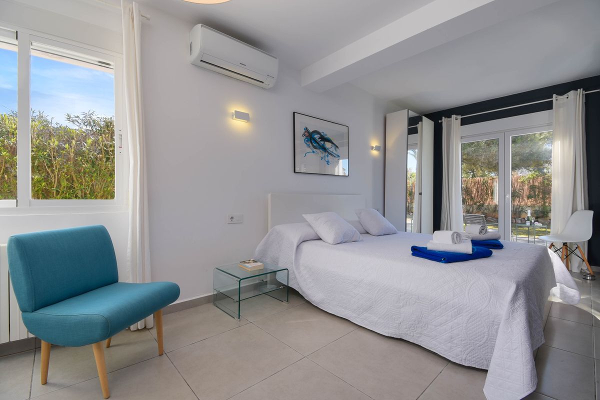 Dormitorio luminoso con cama doble, sillón turquesa y mesita de cristal. Dispone de aire acondicionado, suelos cerámicos y acceso directo al jardín exterior.