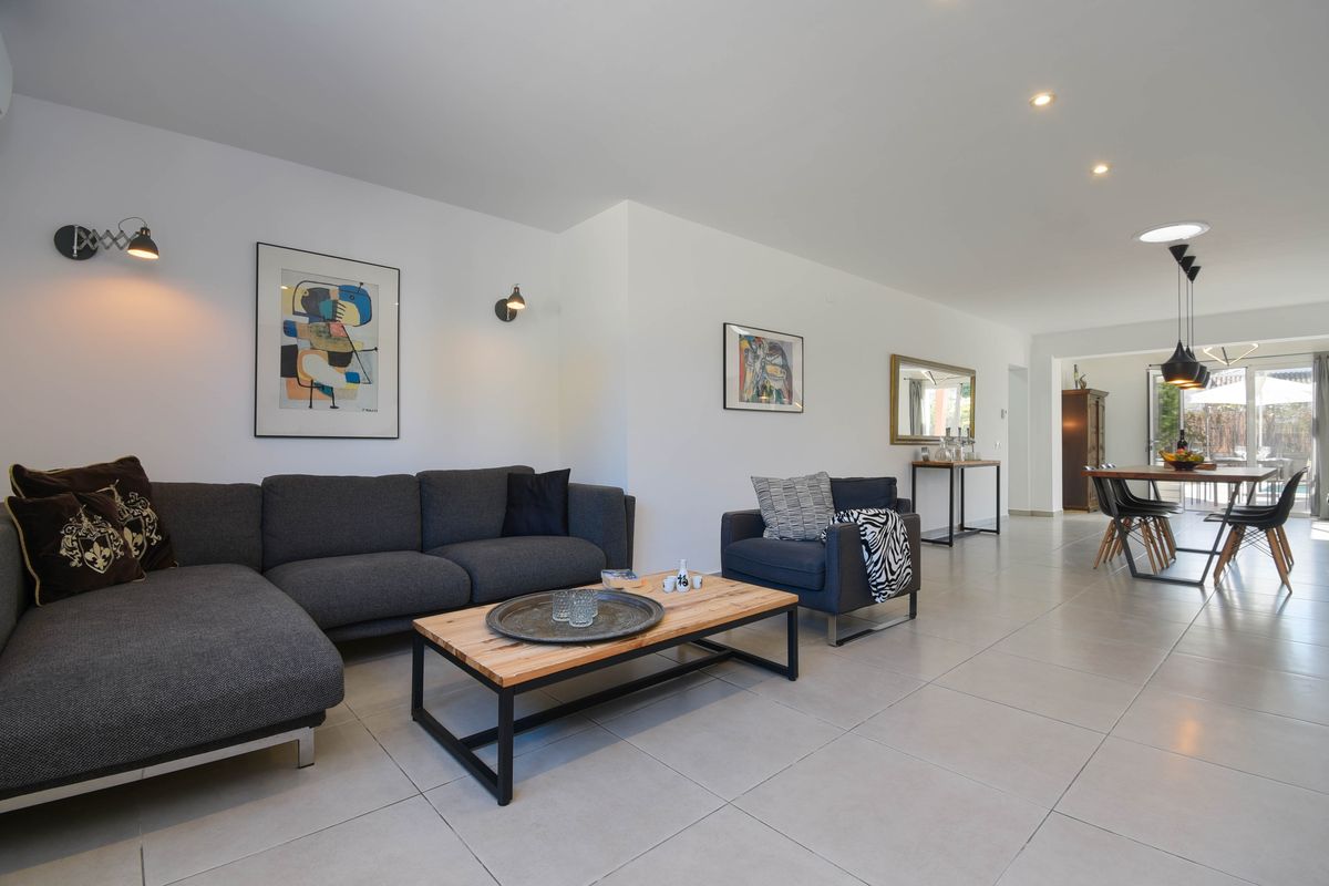 Salón diáfano con sofá modular gris, mesa de centro de madera y metal, y zona de comedor integrada con acceso al exterior.