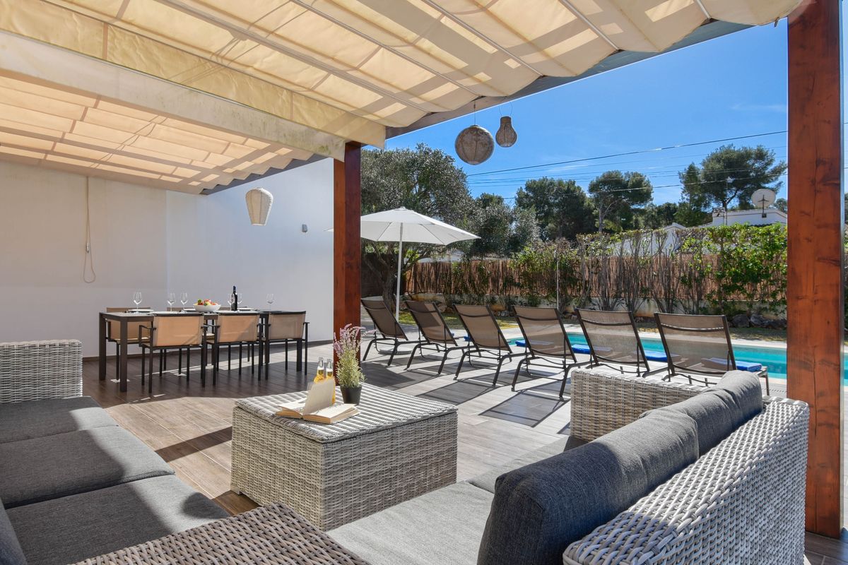 Terraza con toldo retráctil, zona de estar de mimbre, comedor exterior y hamacas junto a una piscina privada rodeada de vegetación.