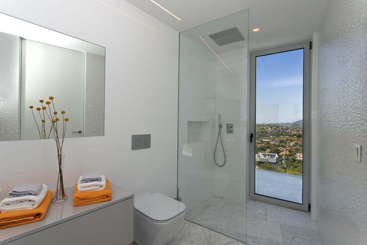 Baño moderno con ducha de obra acristalada, suelo de mármol y acceso directo a una terraza con vistas panorámicas al valle.