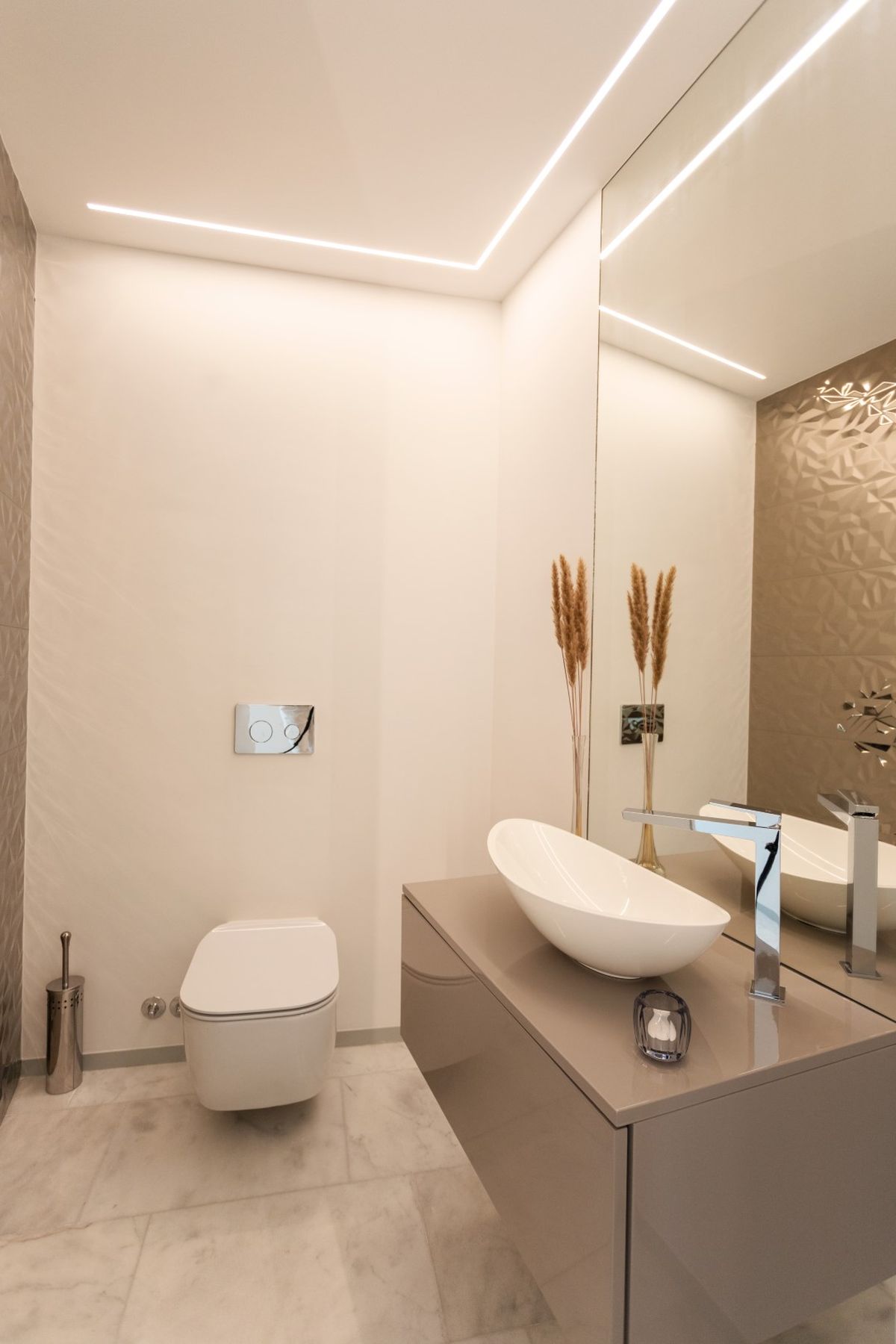 Baño moderno con lavabo ovalado sobre encimera, inodoro suspendido y pared con textura geométrica. La iluminación LED lineal integrada resalta el diseño minimalista.