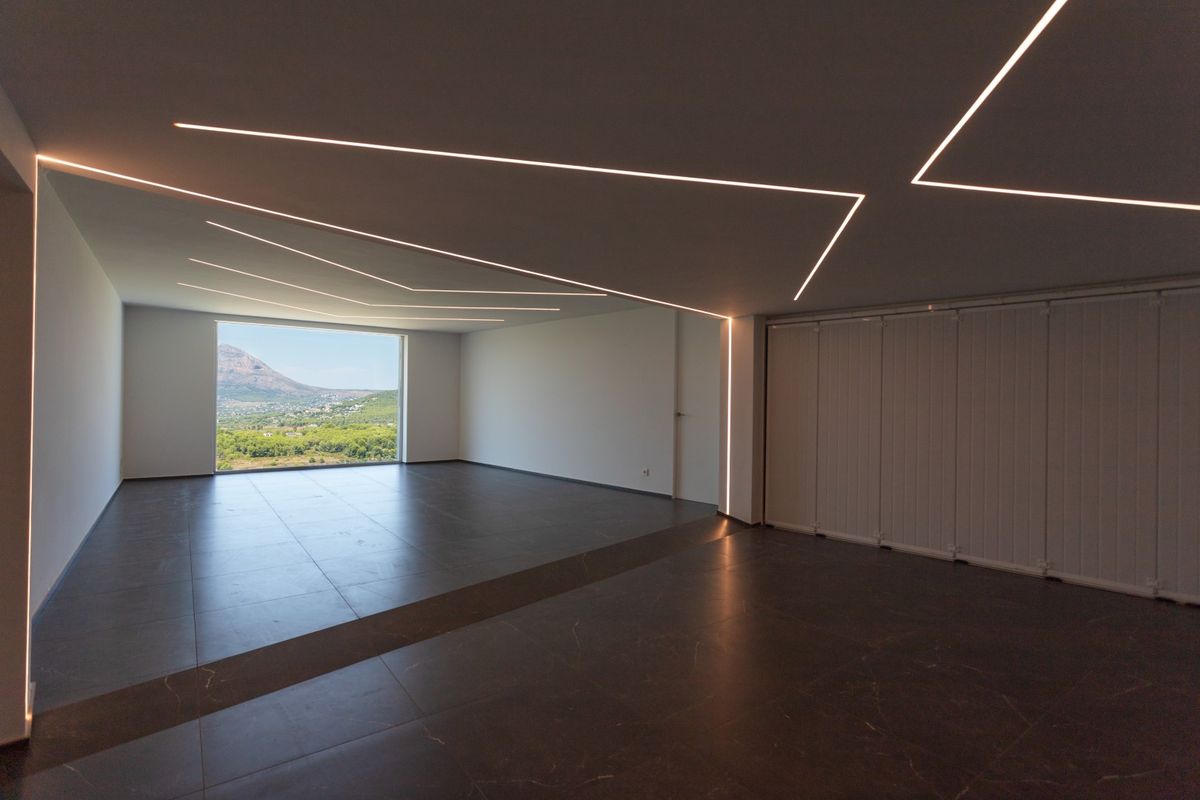 Espacio diáfano con suelo de porcelánico oscuro e iluminación LED geométrica integrada. Un gran ventanal enmarca vistas panorámicas al valle y las montañas.