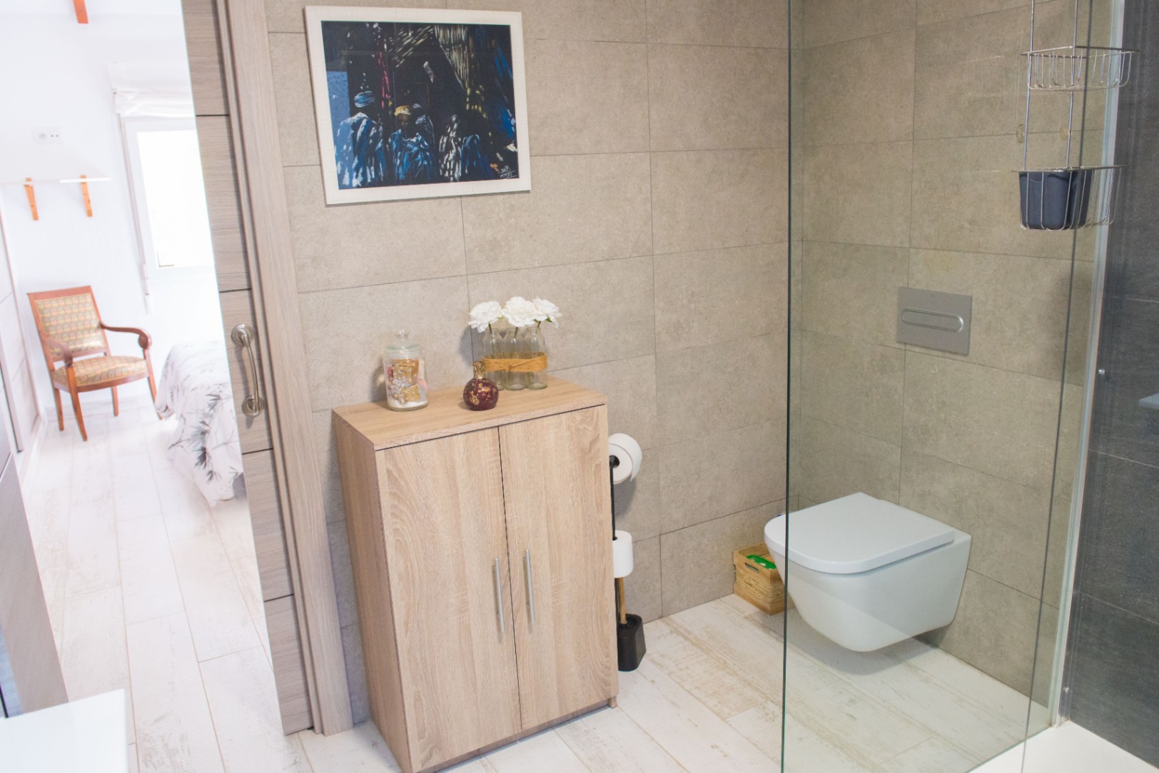 Baño moderno con inodoro suspendido, mampara de cristal y mueble auxiliar de madera clara sobre suelos de gres efecto madera.