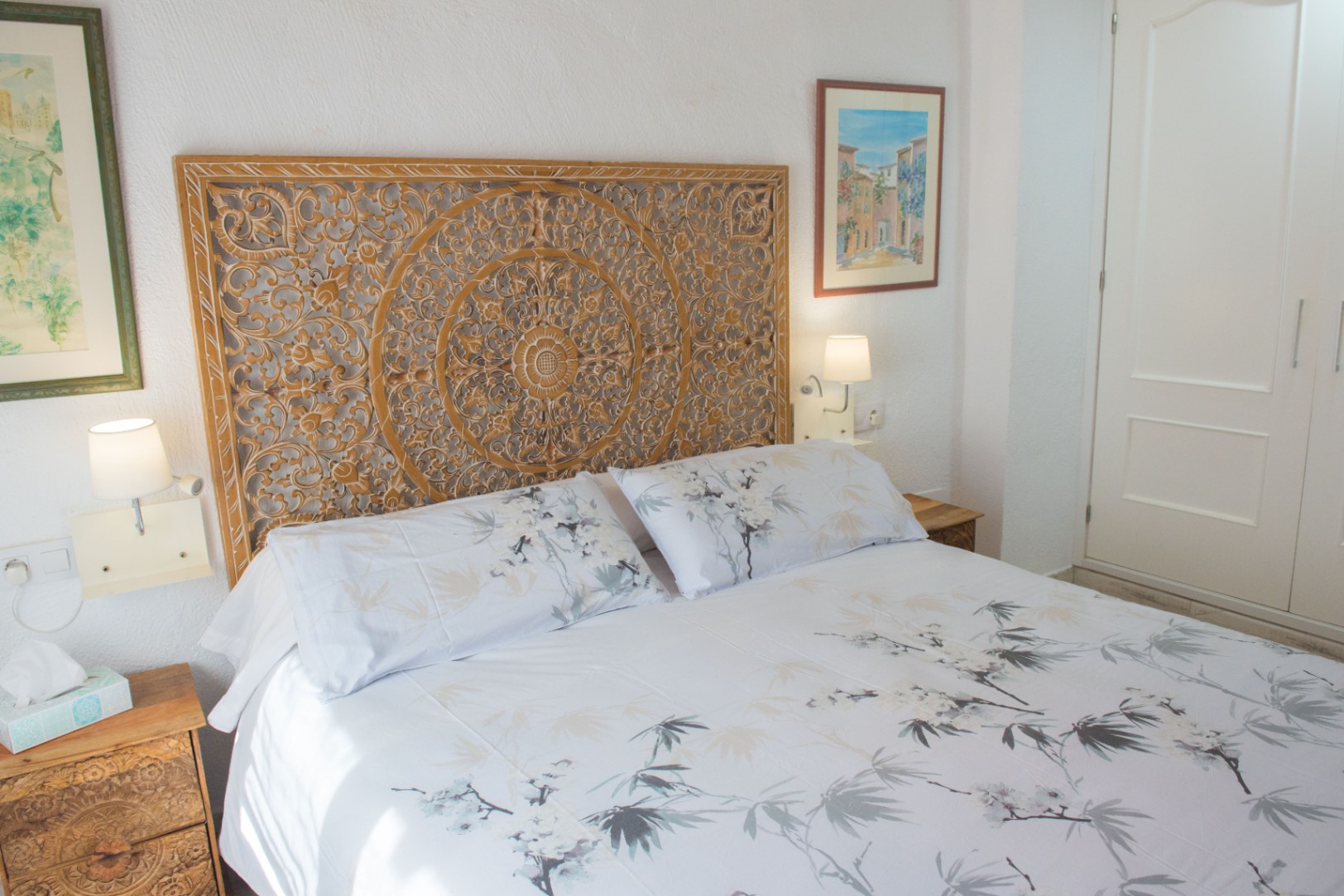 Dormitorio con cabecero de madera tallada a mano, mesitas de noche a juego y lámparas de pared integradas junto a un armario empotrado blanco.