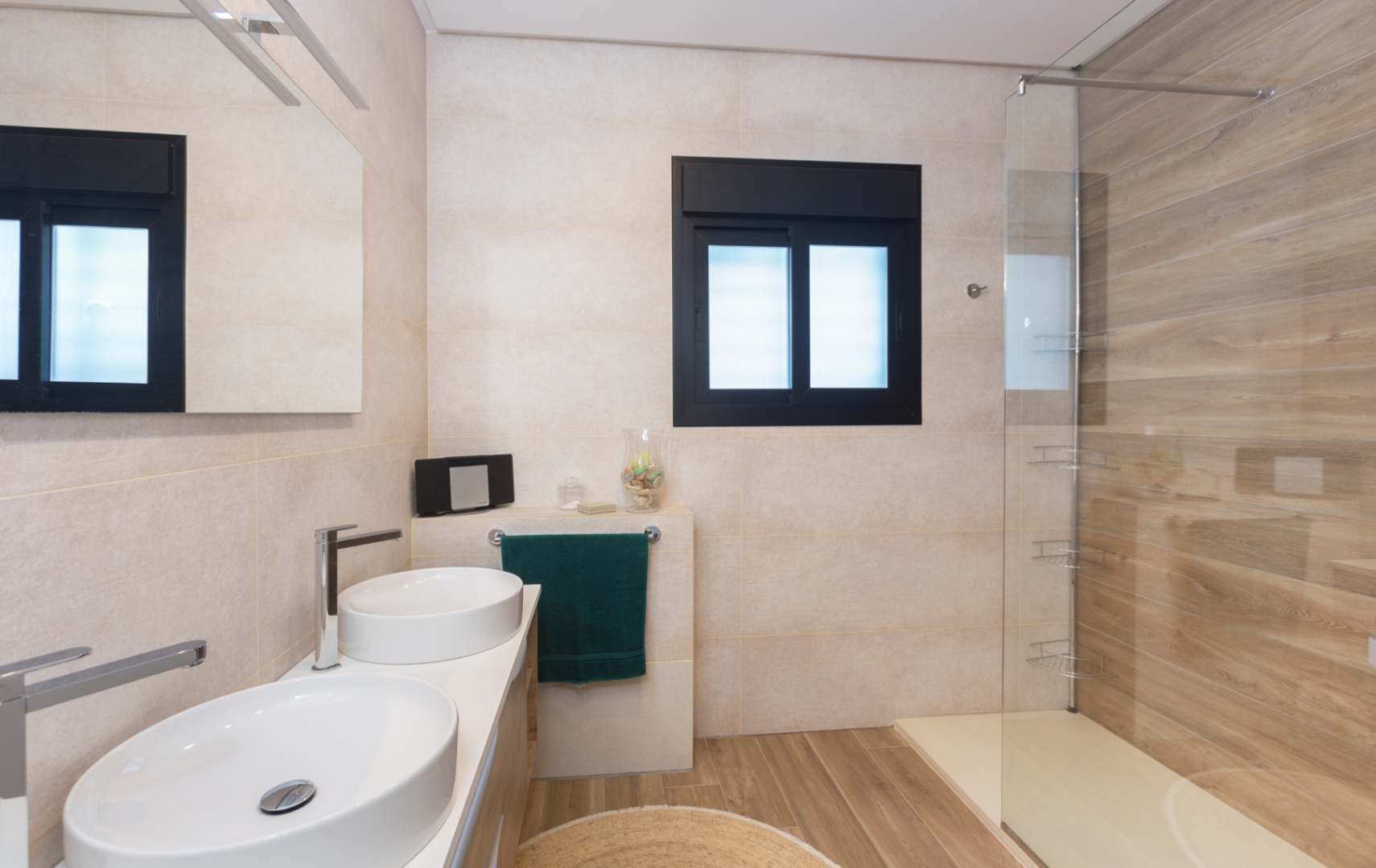 Baño moderno con lavabo de doble seno, revestimientos con efecto madera en la ducha y el suelo, y una mampara de cristal junto a una ventana de marco negro.