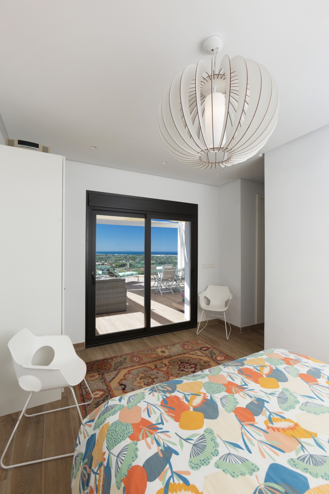 Dormitorio luminoso con acceso directo a la terraza, puertas correderas de marco negro, lámpara de diseño y vistas panorámicas al mar.