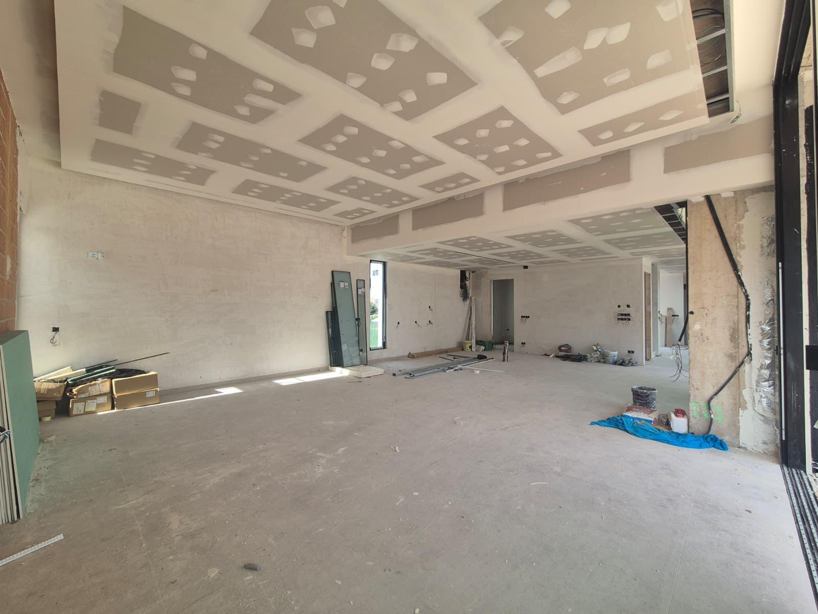 Amplio interior en construcción con techos de placas de yeso a varios niveles para iluminación indirecta y grandes vanos para ventanales de suelo a techo.