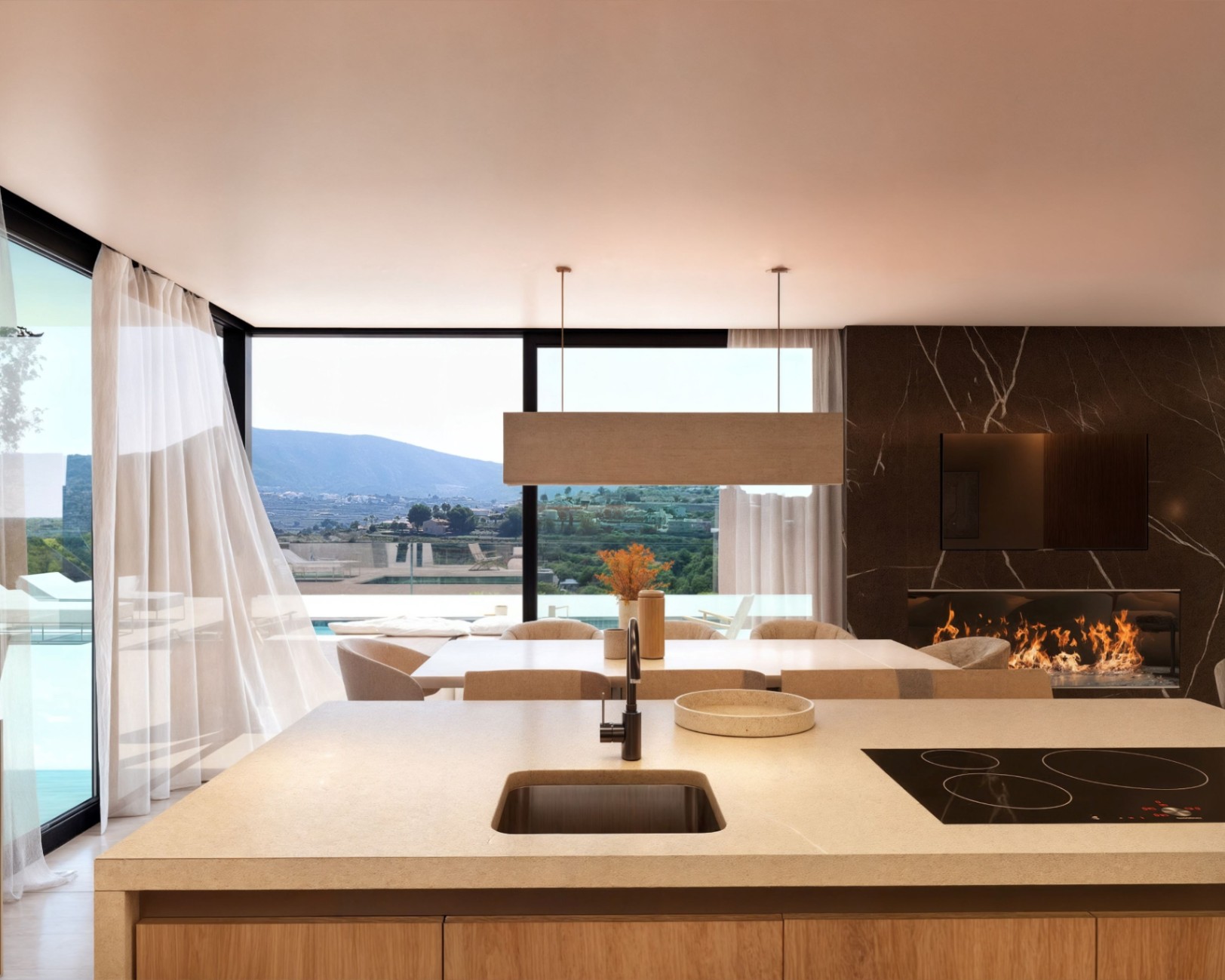 Cocina de concepto abierto con isla de piedra, zona de comedor y salón con chimenea integrada en pared de mármol oscuro y vistas panorámicas al valle.