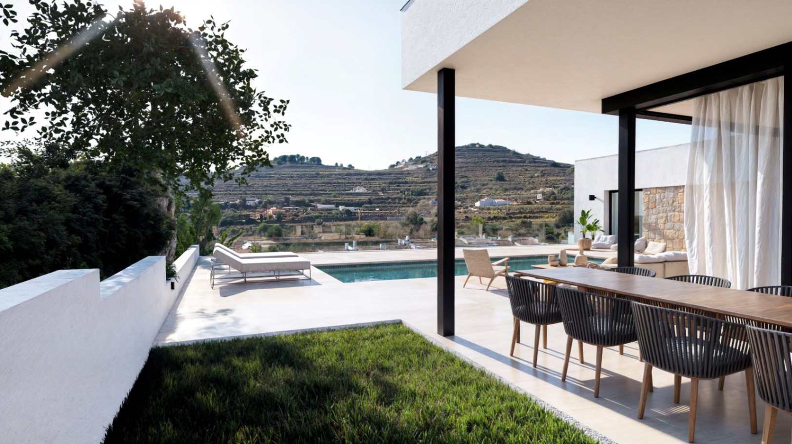 Terraza exterior moderna con comedor de madera, piscina y tumbonas, con vistas despejadas a un paisaje de colinas abancaladas y vegetación mediterránea.