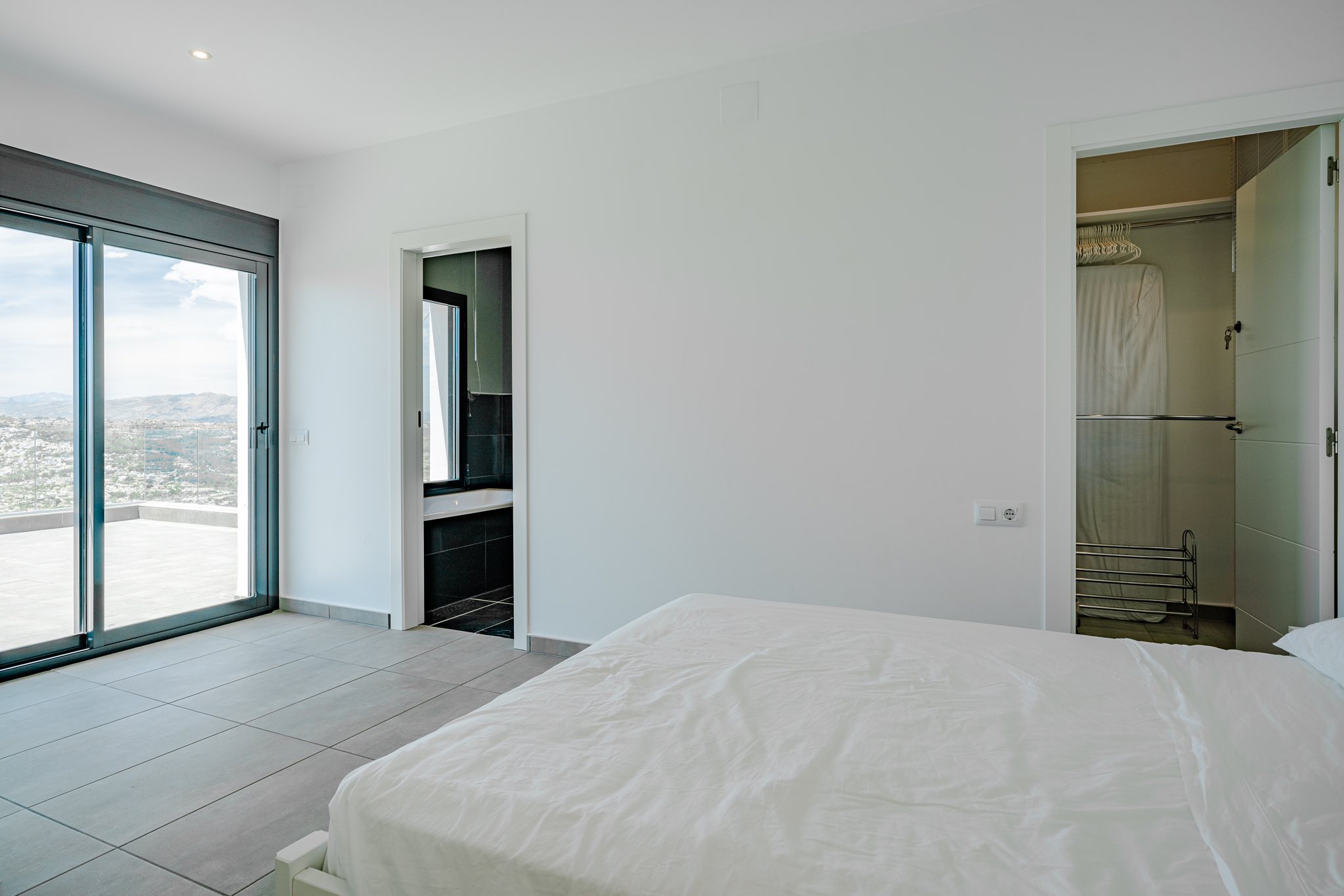 Dormitorio moderno con acceso directo a terraza, baño en suite con azulejos oscuros y un vestidor independiente con suelos de gres gris.