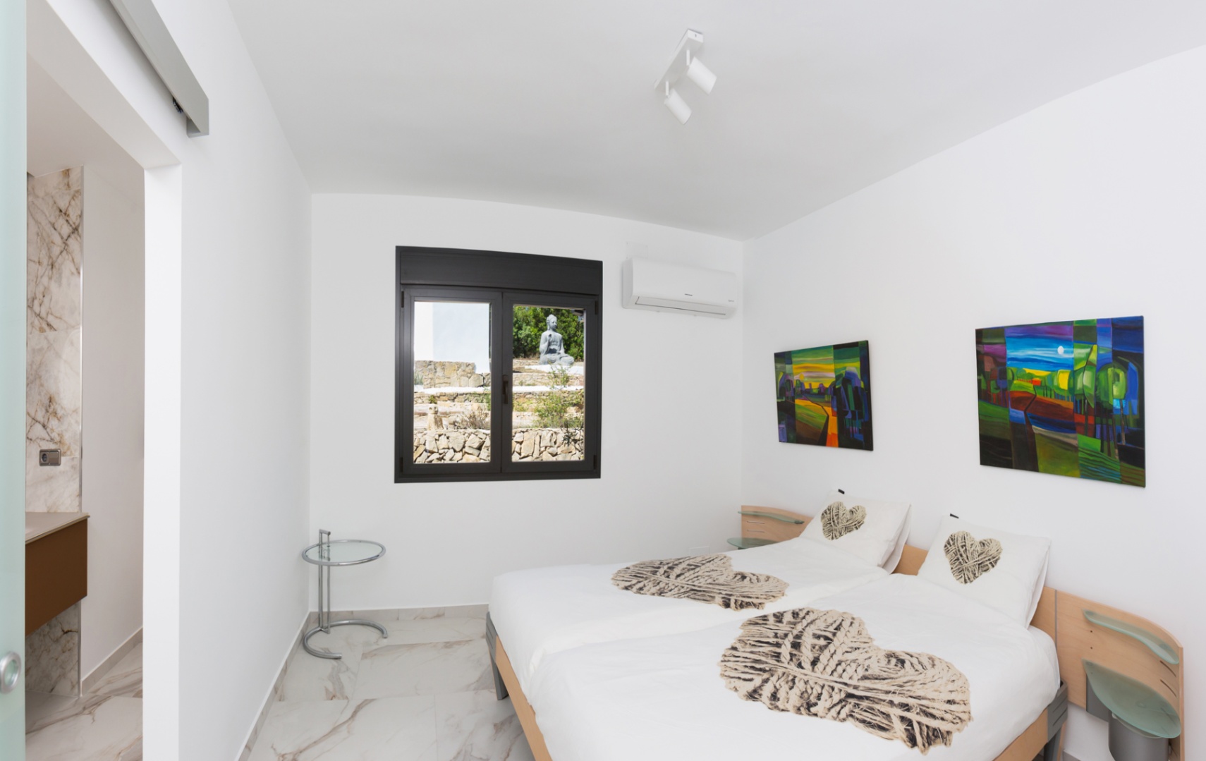 Dormitorio con dos camas individuales, suelos porcelánicos efecto mármol y ventana con vistas a un jardín zen. Incluye aire acondicionado y acceso a baño privado.