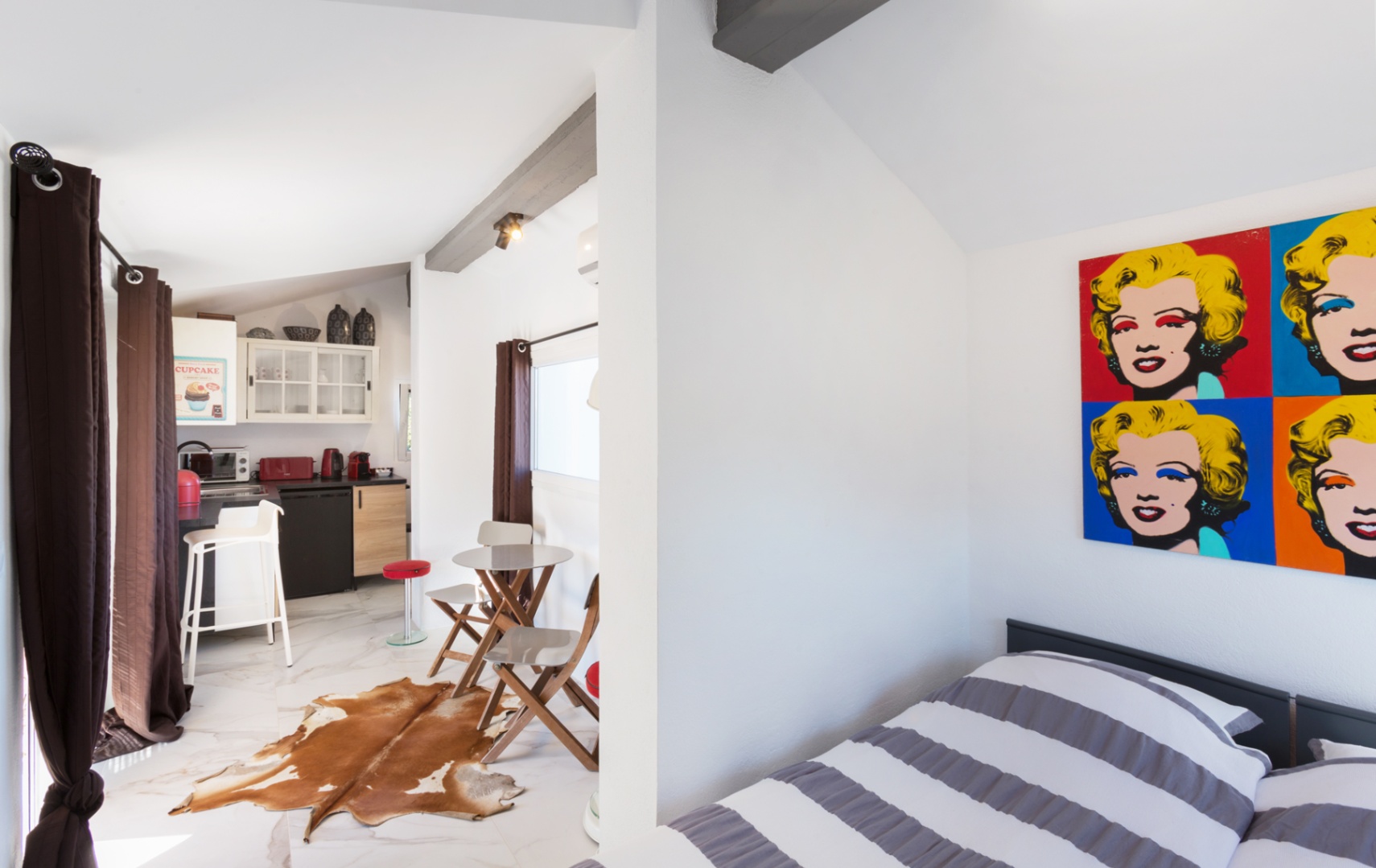 Estudio con decoración pop-art, vigas oscuras y suelo de efecto mármol. Incluye cocina compacta con electrodomésticos rojos y comedor con alfombra de piel natural.